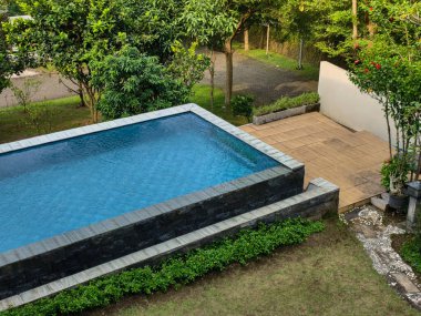 Berrak mavi suyu olan sakin ve davetkar bir yüzme havuzu, canlı, doğal bir manzaranın ortasına kurulmuş..