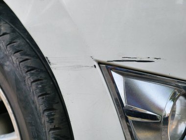 Detailed view of a scratched and dented white car bumper next to a car tire.