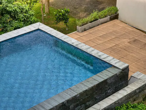 A tranquil swimming pool surrounded by vibrant plants and a warm wooden deck, perfect for relaxation.