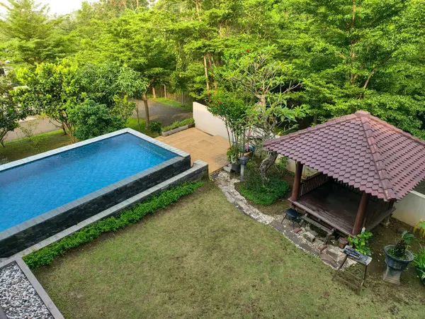 Bereketli tropikal ağaçlarla çevrili, pırıl pırıl mavi yüzme havuzunun sakin havası ve dinlenmek ve tatil için mükemmel, ahşap bir çardak..