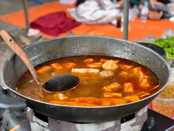 Kaynayan sıcak tencere çorbasıyla dolu büyük bir tavanın yakın plan çekimi, çeşitli malzemeler ve bir kepçe içeriyor..