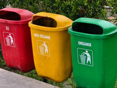 Three distinctively colored bins, red, yellow, and green, are lined up outdoors for waste separation.