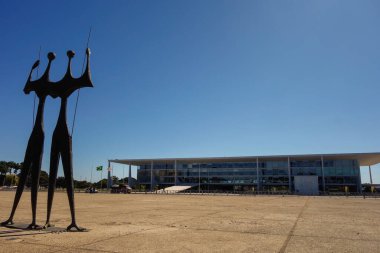 Brasilia, Brazil - Jul 22 2024: sculpture Dois Candangos and Planalto Palace, headquarters of the Presidency of Brazil. clipart