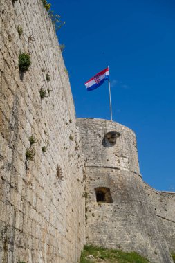 Hırvat bayrağı, Dalmaçya Bölgesi 'nin Hvar adasındaki Hvar kalesinin antik taş duvarının üzerinde dalgalanıyor.