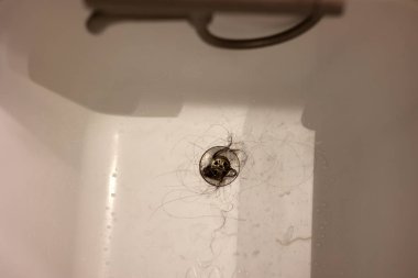The white bathtub sink with lots of dirty hair and dust, the drain is clogged with hair