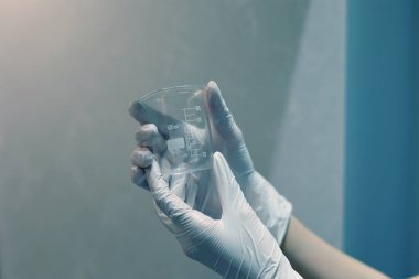 Gloved hands holding an empty beaker in the laboratory