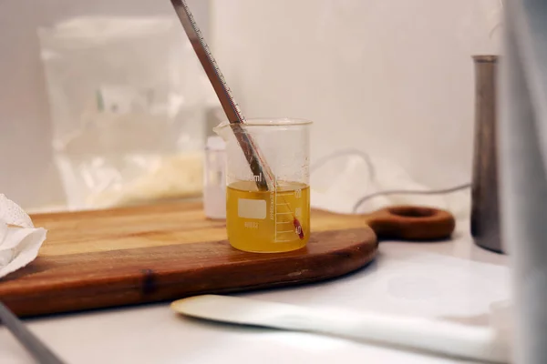The beaker of jojoba oil with thermometer and spoon in the laboratory