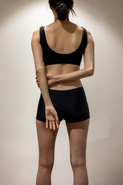 Put arms behind the back, Back view of slim fit female body with black sportswear