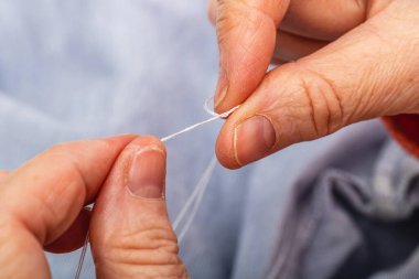 Fotoğraf son derece yatay, elleri yetişkin beyaz kadın, düğümlenmiş iplik. Bir gömleği onarmak için dikiş malzemesi hazırlamak, terzilik yapmak..