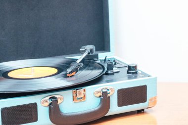 Bavul şeklinde mavi bir pikabın üzerindeki vinil plağın aşırı yakın plan fotoğrafı. Beyaz arka planı olan ahşap bir masada. Uzayı kopyala Kavram hobileri, sanat.