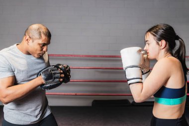 Yatay fotoğraf, beyaz boks eldiveni ve spor giysisi giymiş esmer beyaz kız. Ringde boks hocasıyla yetişkin siyahların ortasında. Spor kavramları, eğlence.