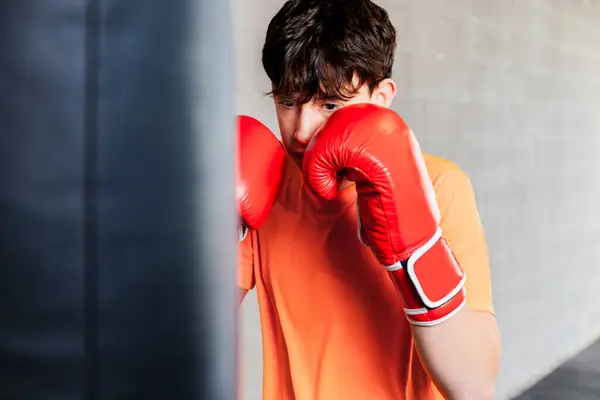 Horizontal photo caucasian teen boy with orange t-shirt and red boxing gloves, in a boxing gym. Copy space. Concept sports, recreation.