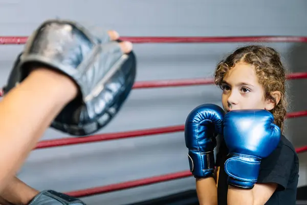 Horizontal photo elementary girl, dressed in black t-shirt and blue boxing gloves, learning boxing in the ring with her teacher. Sport, recreation concept.