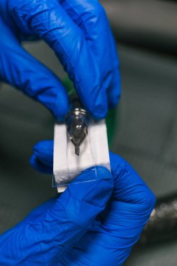 Dikey fotoğraf eldivenli eller titizlikle yeni bir dövme iğnesi hazırladı. Dövme işlemi için sterilizasyon ve hassasiyet sağlıyor. İş dünyası, sanat.