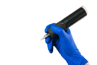 Mavi eldivenli, yatay dövmeli bir sanatçının elinde beyaza izole edilmiş, sanat yaratmaya hazır olduğunu sembolize eden bir dövme makinesi var. Uzayı kopyala İş dünyası, sanat.