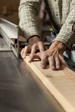 Bir marangozun elindeki dikey fotoğraf, tahta bir tahtayı testerenin çitine karşı güvenli bir şekilde yönlendirirken güvenlik ve doğruluğu vurguluyor. Uzayı kopyala İş konsepti.