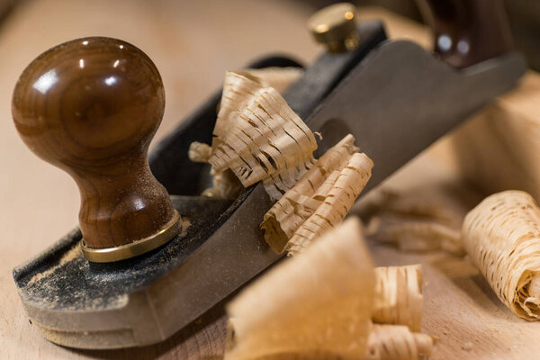 Horizontal photo close-up of an antique hand plane on a wooden surface, surrounded by delicate wood shavings, highlighting fine craftsmanship. Business concept.