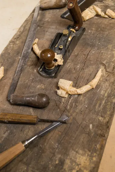 Vertical photo detailed close-up of woodworking hand tools, including chisels and a vintage hand plane, on an aged workbench with fresh shavings. Business concept.