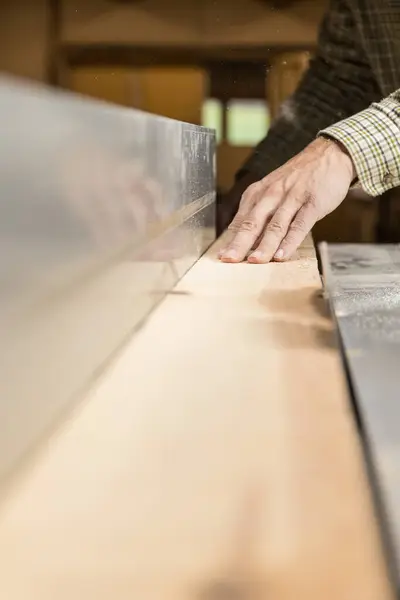 Vertical photo a master carpenter\'s hands demonstrate control and precision while guiding a plank of wood through the sharp blade of a table saw. Business concept.