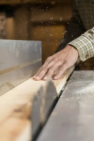 Vertical photo in the midst of sawing, a carpenter\'s hands expertly guide wood through a table saw, with sawdust particles dancing in the workshop light. Business concept.