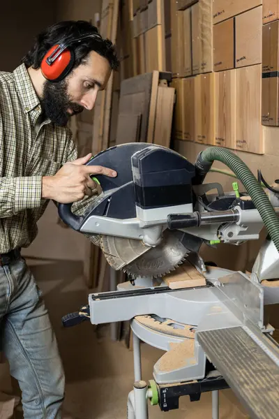 Vertical photo A focused carpenter is seen cutting a wooden plank with a miter saw, taking care to make a precise angle cut. Business concept.