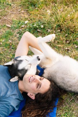 Vertical photo laughter fills the air as a man with curly hair and his playful husky share a moment of pure bliss, lying on the grass together. Lifestyle concept. clipart