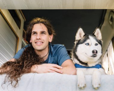 Bir adam ve iri yarı akranının karavanından yatay bir fotoğraf. Macera ruhunu somutlaştıran yolculuklarının bir sonraki ayağı için sabırsızlıkla bekliyorlar. Yaşam tarzı kavramı.