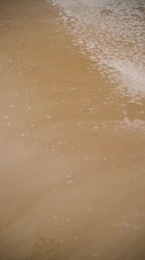 Yavaş çekim dikey video 1080 yakalama okyanus köpük nazikçe kumlu kıyıda yıkanan, arka planda deniz sakinleştirici ses. Sükunet ve dingin ortamı vurguluyor