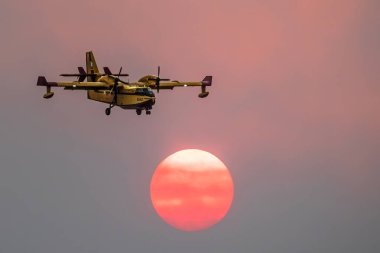 Aleksandropolis Evros Yunanistan 'daki yıkıcı orman yangını, su bombardıman uçakları silueti, dumanlar gökyüzünü kapladı, günbatımı renkleri.
