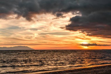 Kumsalda romantik bir gün batımı. Bulutlu bir gökyüzü, bir resim gibi, Samothrace adasına bakıyor..