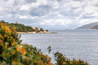 Preveza yakınlarındaki İyon Denizi 'ndeki Fiskardo Kefalonia Yunan adasına seyahat edin. Yaz tatili. Bulutlu gökyüzü ve ön planda kırmızı çiçekler.