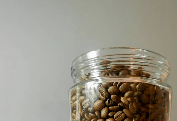 A glass container filled with roasted coffee beans on a warm grey background