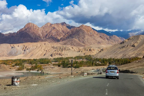 Rural road in north India with a mountain backdrop in winter. High mountains and cedar forests change color in rural winter travel. Leh Ladakh countryside of India.