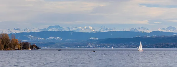 Yacht sailing across Lake Zurich in sunset moment with snow capped mountain in late winter.A beautiful Panorama landscape of lake in Zurich , Switzerland. People doing activity.Swiss apls background.