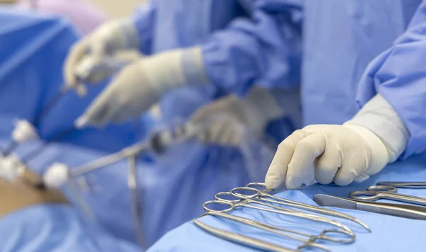 Scrub nurse picking up surgical instruments for surgeon inside operating room in modern hospital.Doctor in blue protective uniform doing laparoscopic surgery.Selective focus with blur background.