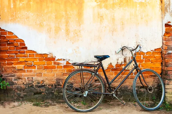 A vintage bicycle lay down on the wall. Old wall was cracked and the orange bricks were exposed.Old-style bicycles with yellow wall background.Yellow color was painted onto the wall vintage style.