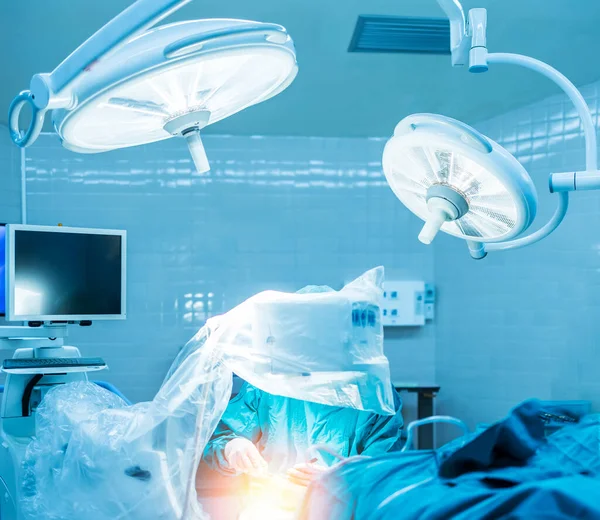 Doctor doing surgery under fluoroscopy with monitor inside orthopedic operating room in hospital. Blue tone color of operating theater with orange light effect.Medical concept.Surgeon working hard.