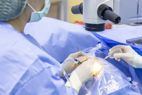 Doctor doing surgery inside modern operating theater in surgical hospital.Microscope was use in eye surgery.Surgeon in blue sterile suit working with microscope with light effect.Medical concept.