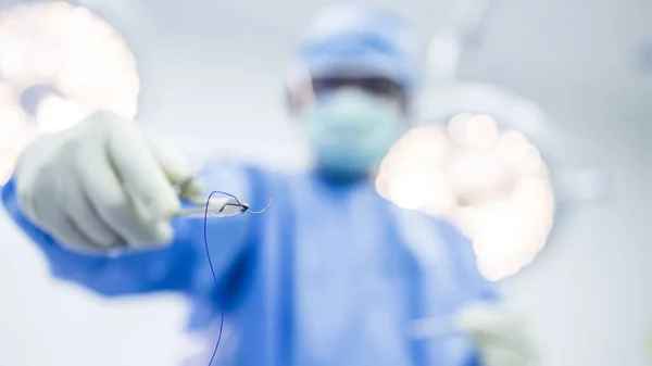 Selective focus on surgical needle holder with blur background.Surgeon or doctor inside operating room did suture while surgery in hospital.Orthopedic or cosmetic and surgical emergency surgery.
