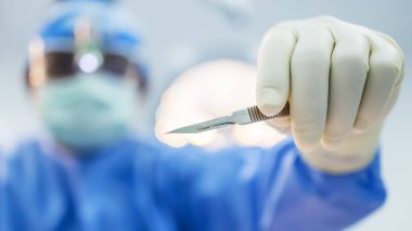 Bulanık geçmişi olan cerrahın eline seçici bir odaklanma. Doktor ya da cerrah, ameliyat için kullanılan ameliyat odasının içinde yükselen açıyla deri kesiği yaptı..
