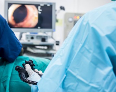 Açık mavi önlüklü bir doktor ya da cerrah hastanedeki ameliyathanede kolonoskopi ya da gastroskopi yaptı. Kanser taraması için EGD teknolojisi. Bulanık yeşil arka plan ve ön plan..
