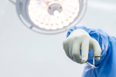 Hastanedeki bir ameliyathanede elinde tıbbi makas aleti olan mavi üniformalı doktor ya da cerrahlara yakın çekim. İnsanlar beyaz arka plan boşluğuna sahip cerrahi lamba teknolojisi cihazı altında ameliyat yaptılar..