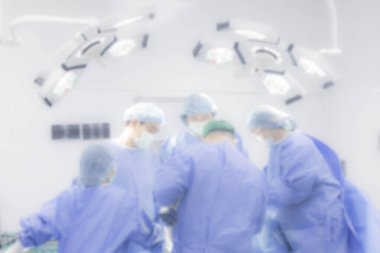 Geçmişi bulanık ya da bulanık. Mavi üniformalı bir doktor ekibi ameliyat odasında cerrahi lamba teknolojisiyle. Beyaz bulanık arka plan. Klinikte çalışan tıbbi grup. Ortopedik birim..