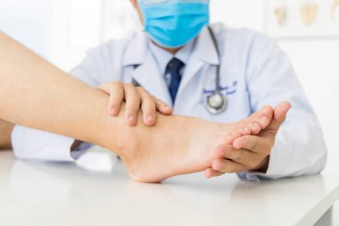 Beyaz önlüklü ortopedi doktoru ya da cerrah, ayağı ağrıyan hastayı muayene etti. Beyaz masa ya da bulanık arka planı olan bir yatak. Metatarsalgiye bulaşmış hallux ya da nasır. Ortopedik birim.