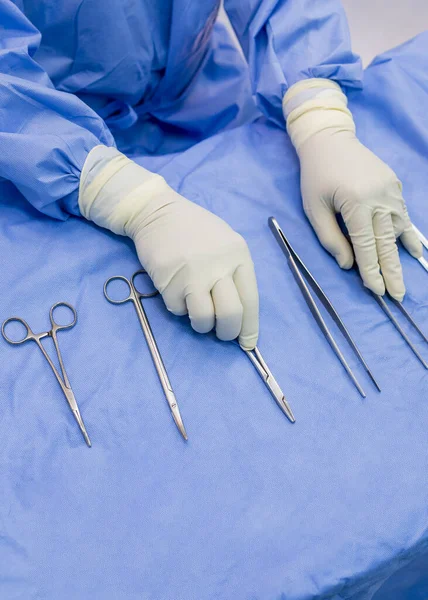 stock image Surgical nurse or surgeon holding medical forceps or instrument inside operating room on blue table.Metal or stainless tool for surgery.Doctor with latex or rubber glove.Hand of surgeon.