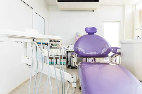 Violet dental chair with white dental unit in clinic or hospital with nobody.Empty dental room for toothache or orthodontic patient.Dentist \'s workplace.Medern technology for root treatment.