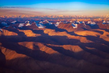 Winter aerial landscape of snow cap mountain in sunrise. Karakorum or Himalaya mountain from above in morning.Sunlight touch the peak of summit with clear blue sky.Mountain in Leh Ladakh,India.