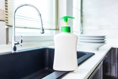 Mutfak lavabosunda bulaşık deterjanı ve arka planda temiz tabaklar. Bulaşık deterjanı, modern tasarım mutfağı ve su musluğunun penceresinin yanındaki yazı için boş veya beyaz etiketli sıvı şişe..
