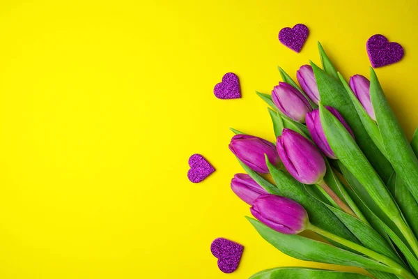 Bouquet of purple tulips with hearts on yellow background. Mothers day, Valentines Day, Birthday celebration concept. Greeting card. Copy space, top view.