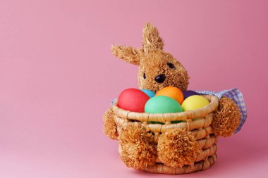 Straw bunny basket with easter colorful eggs on pink background. Happy Easter. Copy space. Close up.